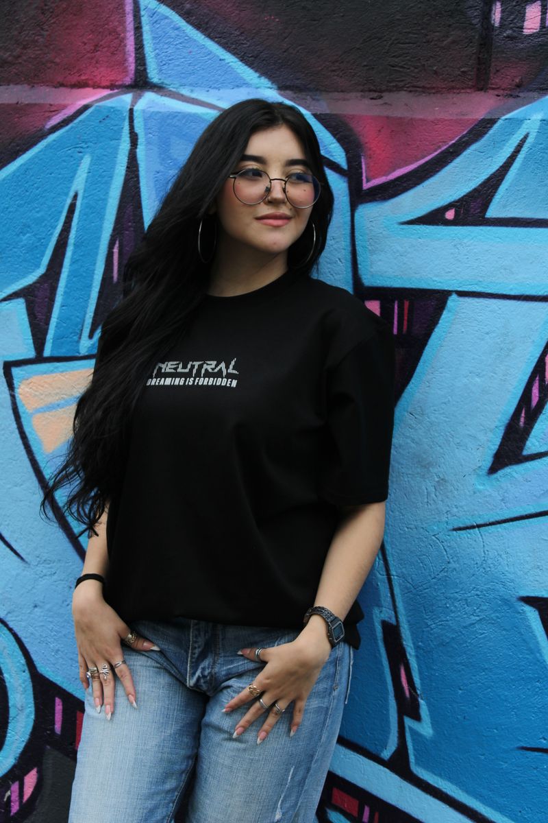 Modelo con camiseta oversize negra del catálogo frente a un mural